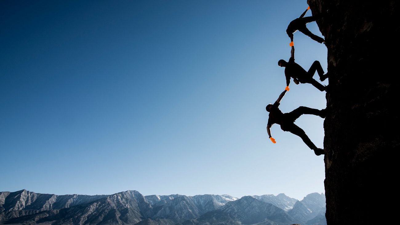 Bergsteiger an einer steilen Wand, die sich gegenseitig Kletterhilfe geben